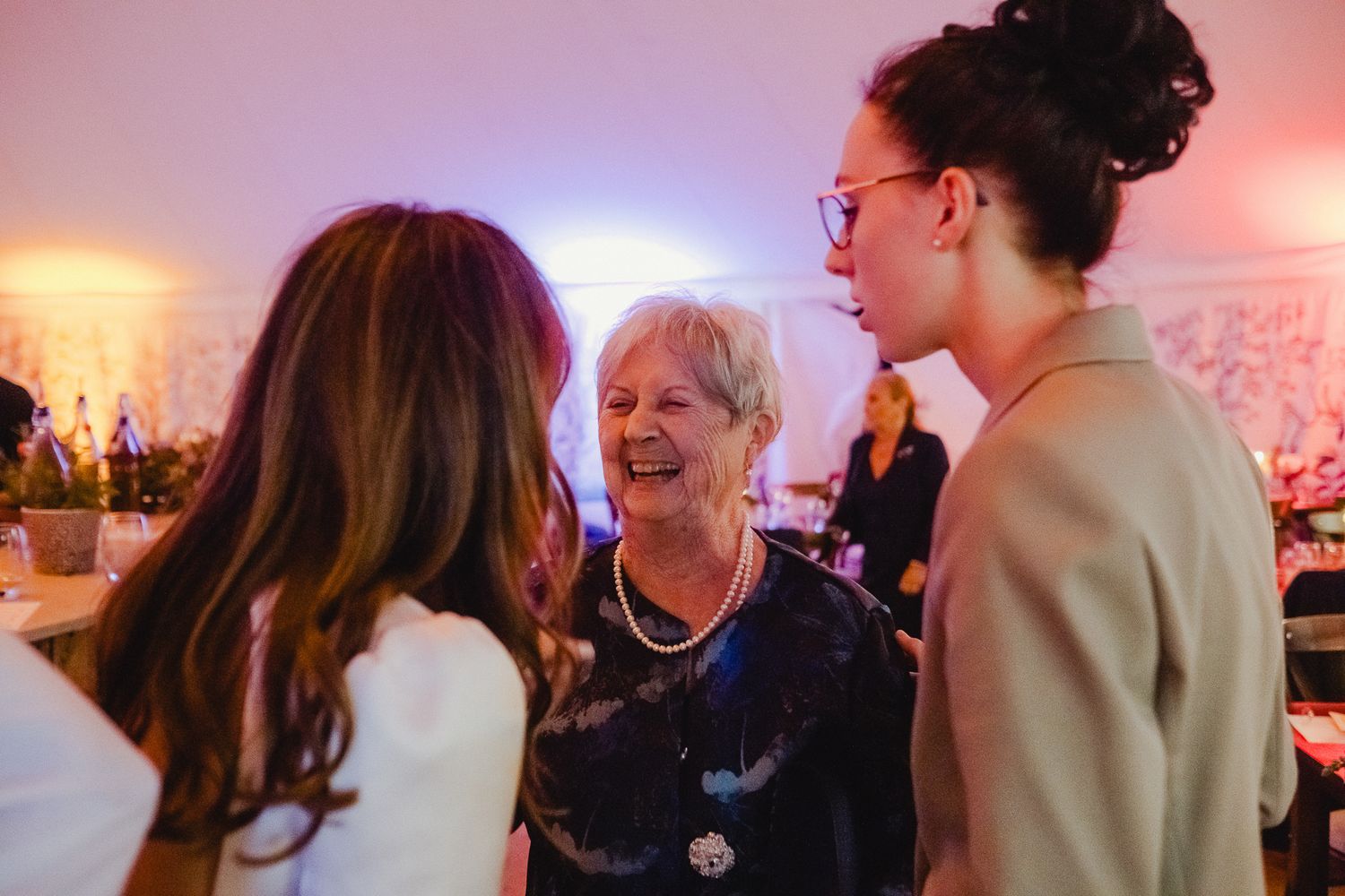 Wedding guests dancing and socializing at a lively reception with warm red lighting and a festive atmosphere.