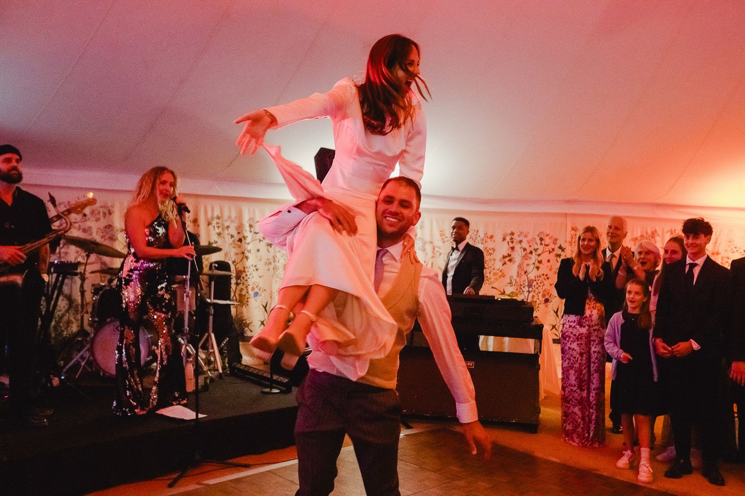 Couples dance together at a wedding reception illuminated by warm red lighting on the dance floor.