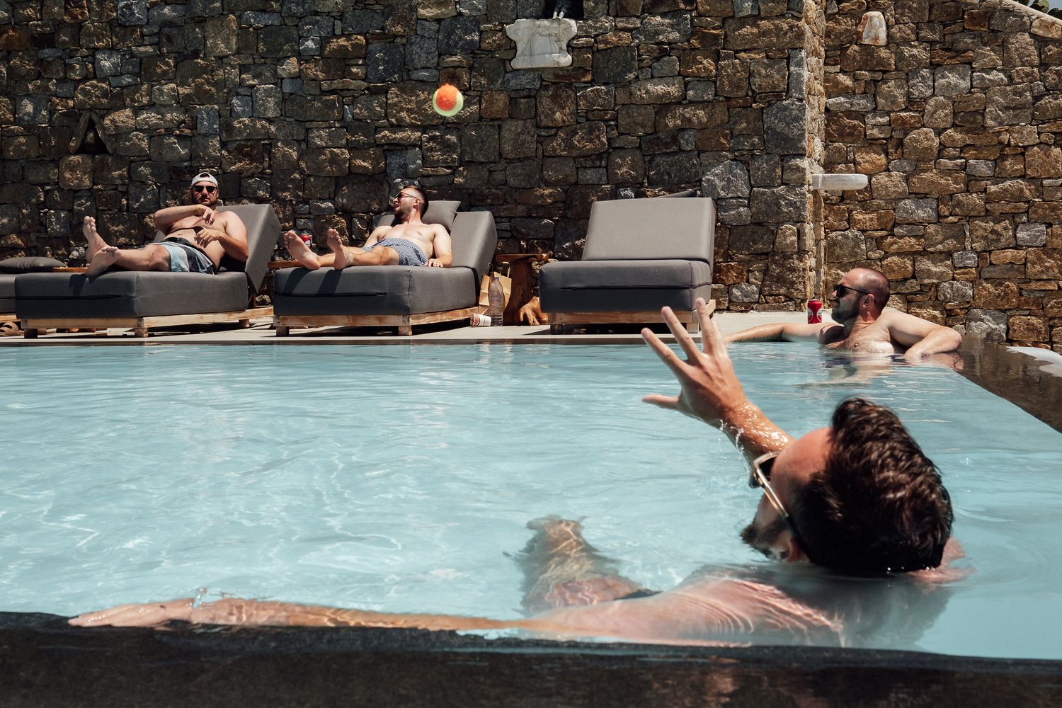 People relaxing by a pool with stone walls, lounging on chairs and swimming on a sunny day.