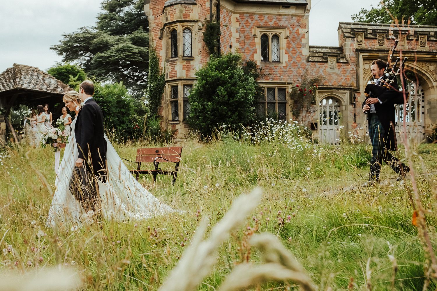 Newlyweds pose in overgrown grass with Gothic-style mansion in background.