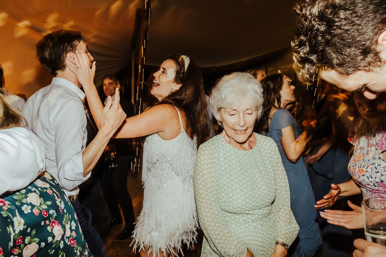 Wedding guests dance joyfully at a lively reception with warm lighting and festive atmosphere.