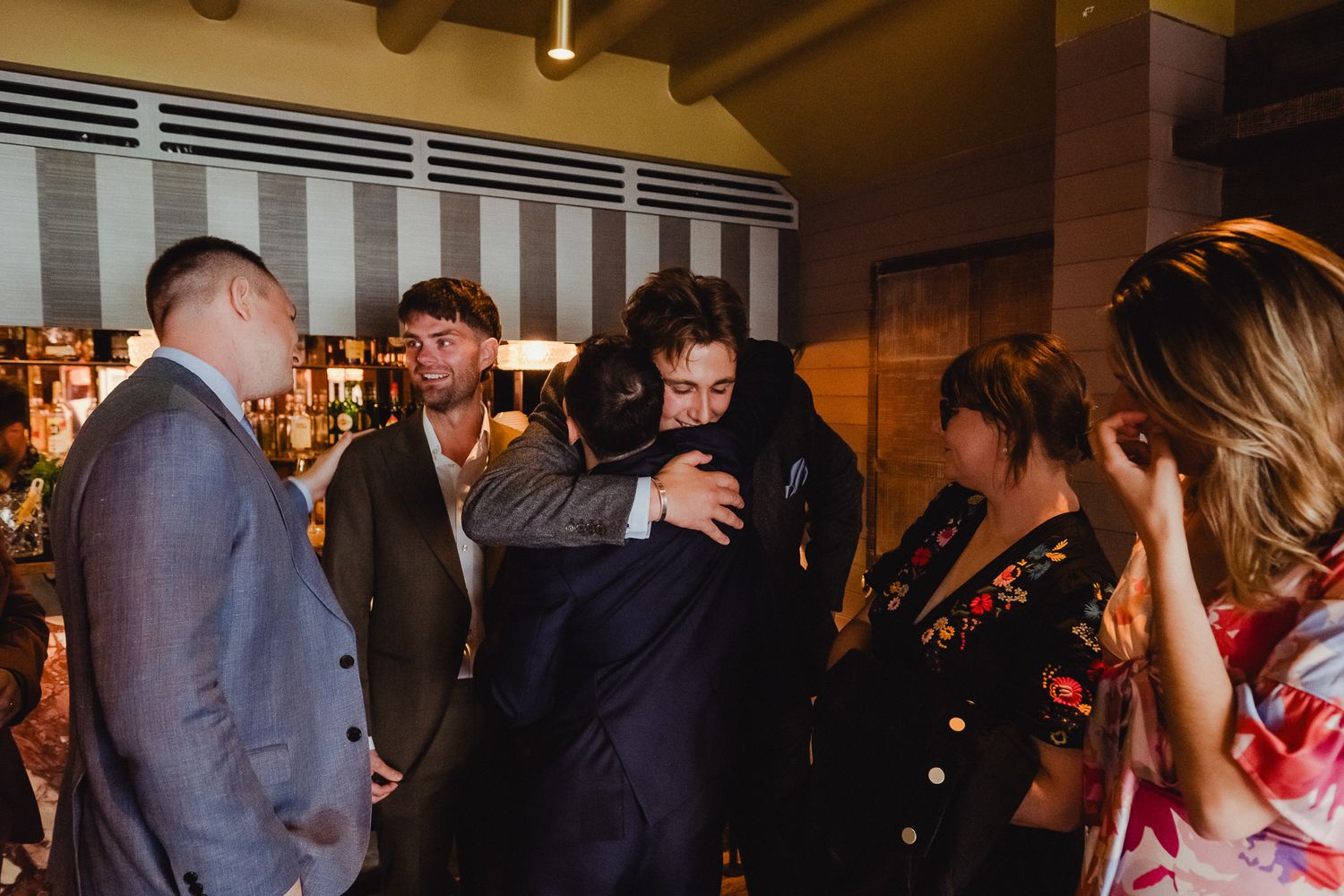 A crowded dance floor at a wedding reception with people dancing and socializing in a dimly lit venue.