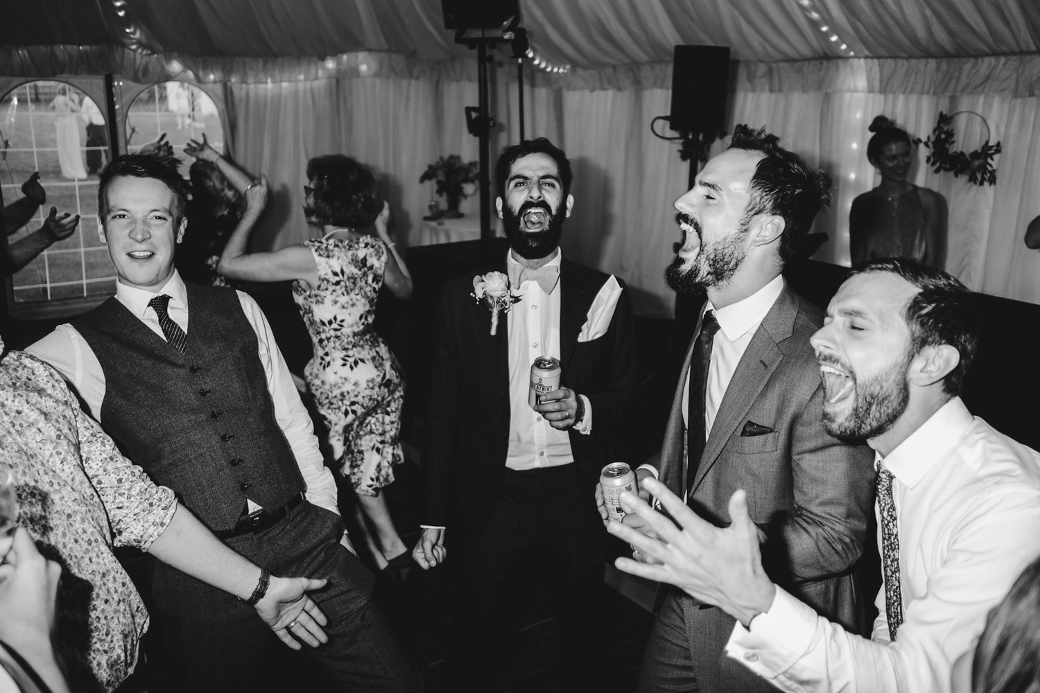 Wedding reception guests mingling and dancing in a large tented venue space.