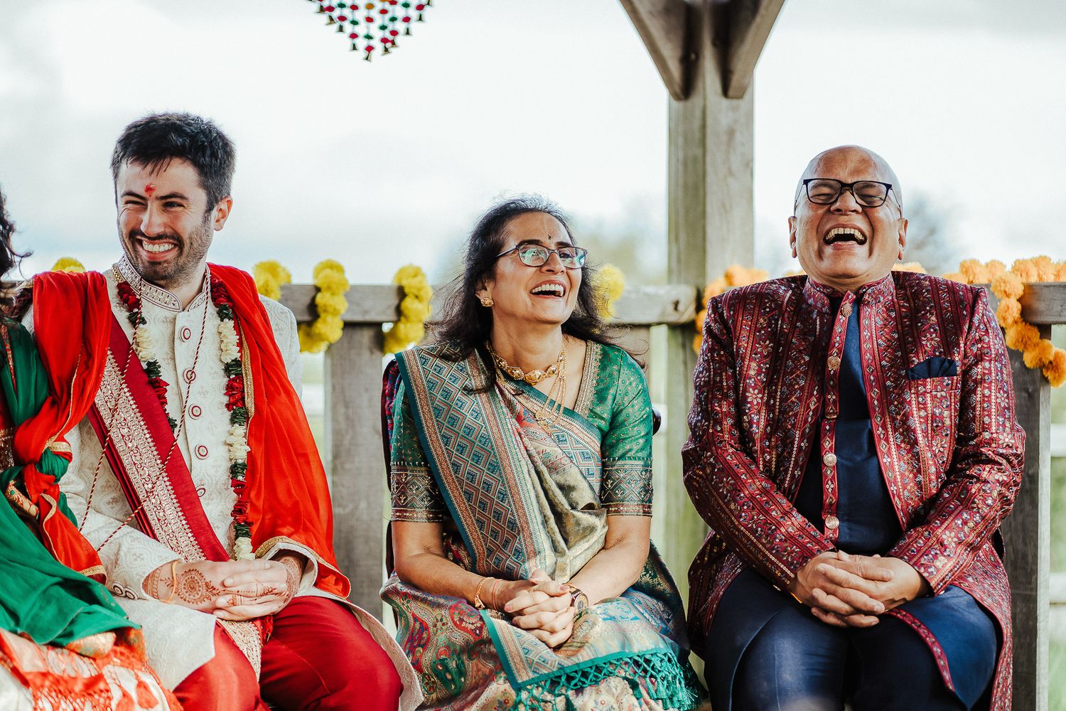 Three people in colorful traditional Indian attire sharing a joyful moment at an outdoor celebration.