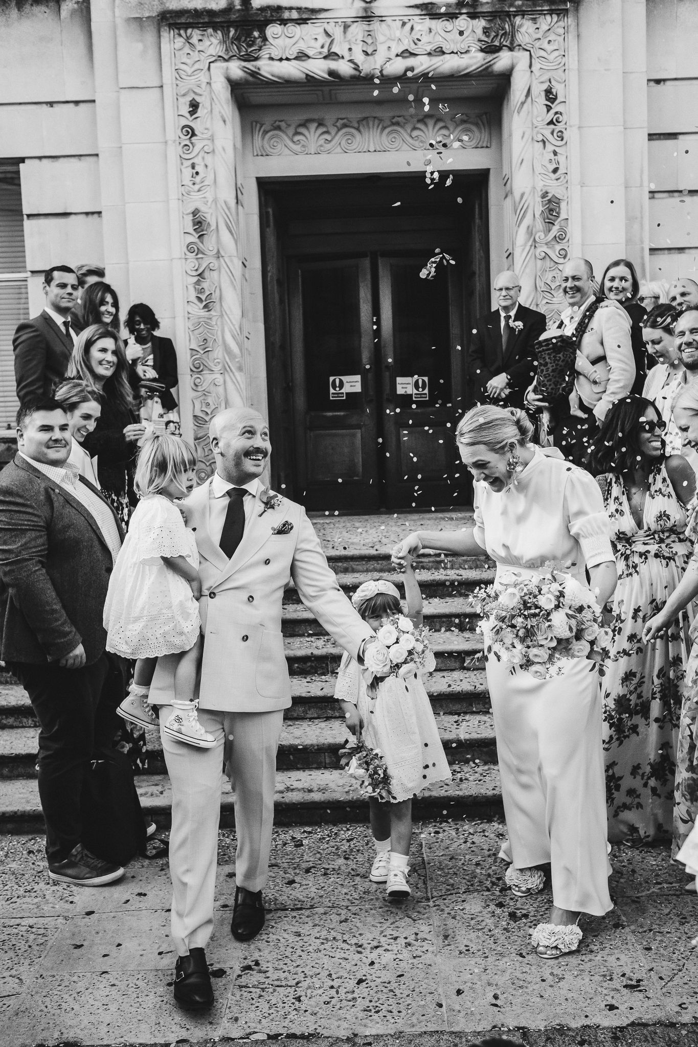 Wedding party celebrating with confetti outside a classic building entrance.