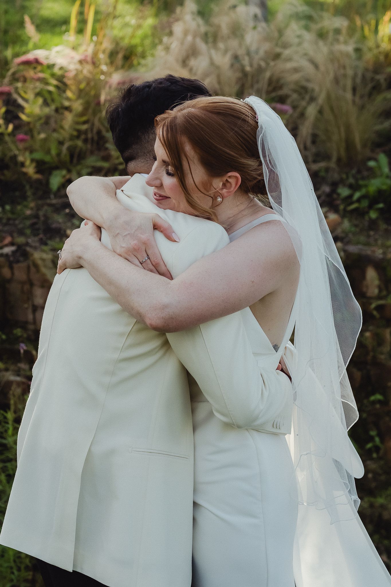 A tender embrace between two people in white attire during an outdoor wedding ceremony.