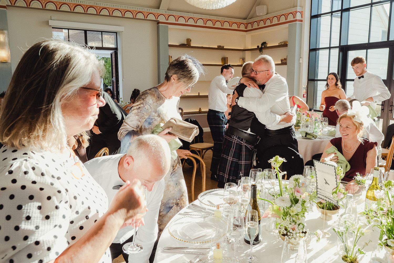 People gathered at an elegant dining table with white flowers and glassware during a celebratory event.