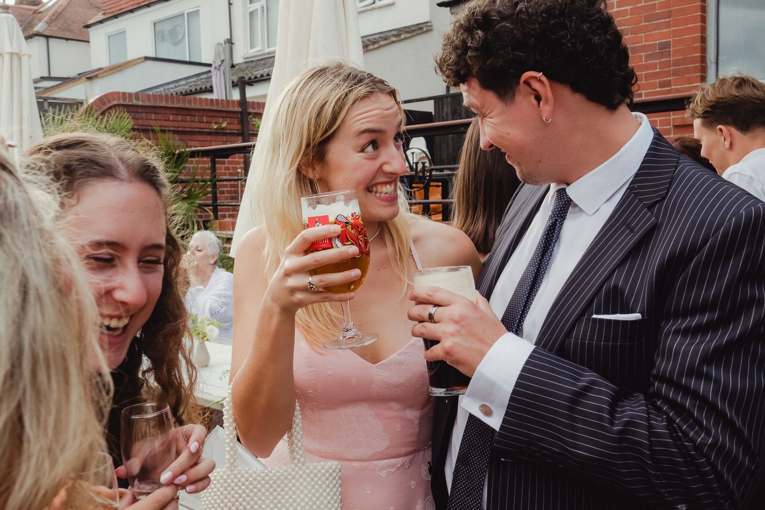Wedding party guests in formal attire gather for drinks and conversation at an outdoor reception.