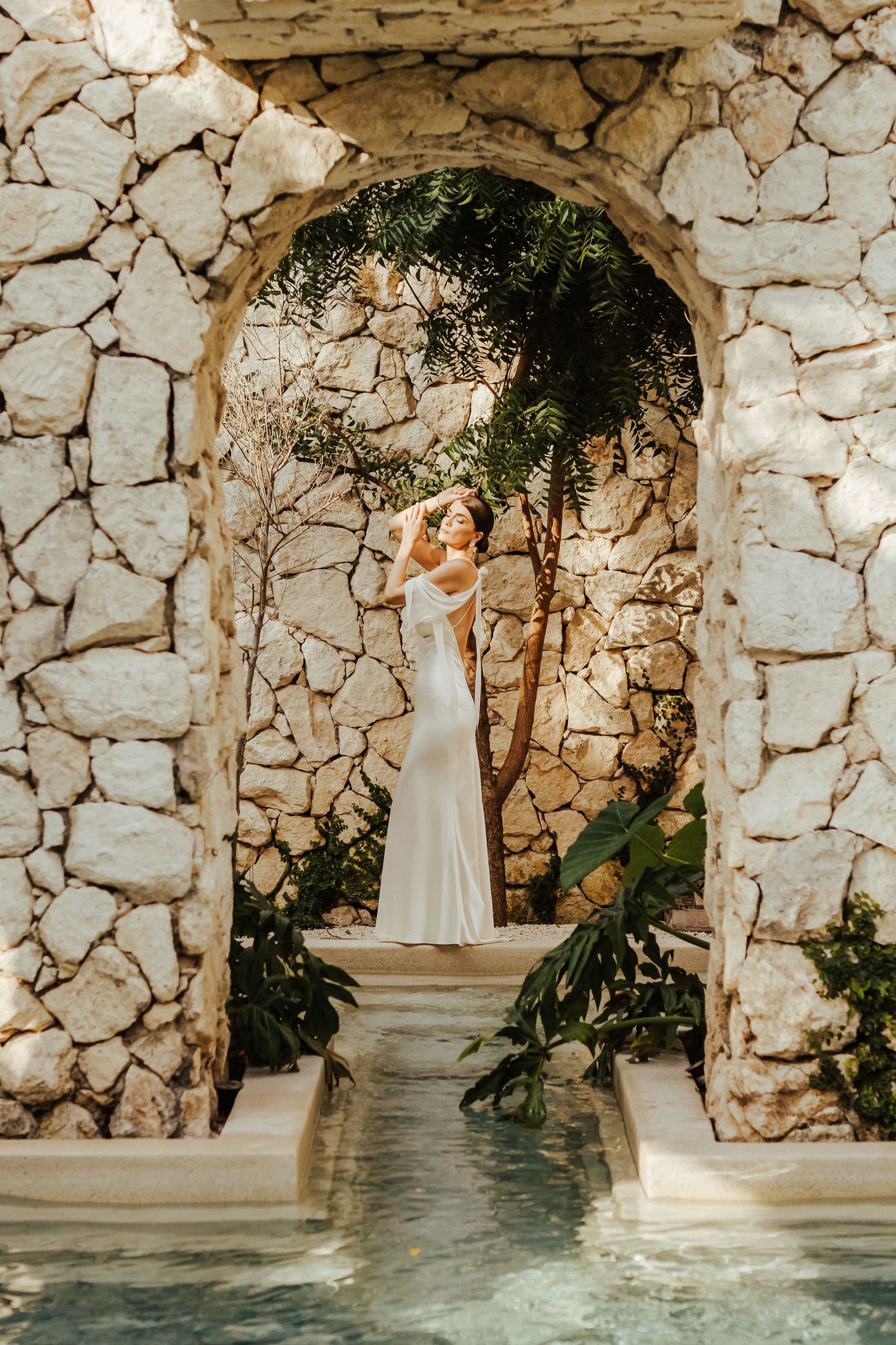 A white stone archway frames a pool entrance at a luxury resort with lush tropical greenery.