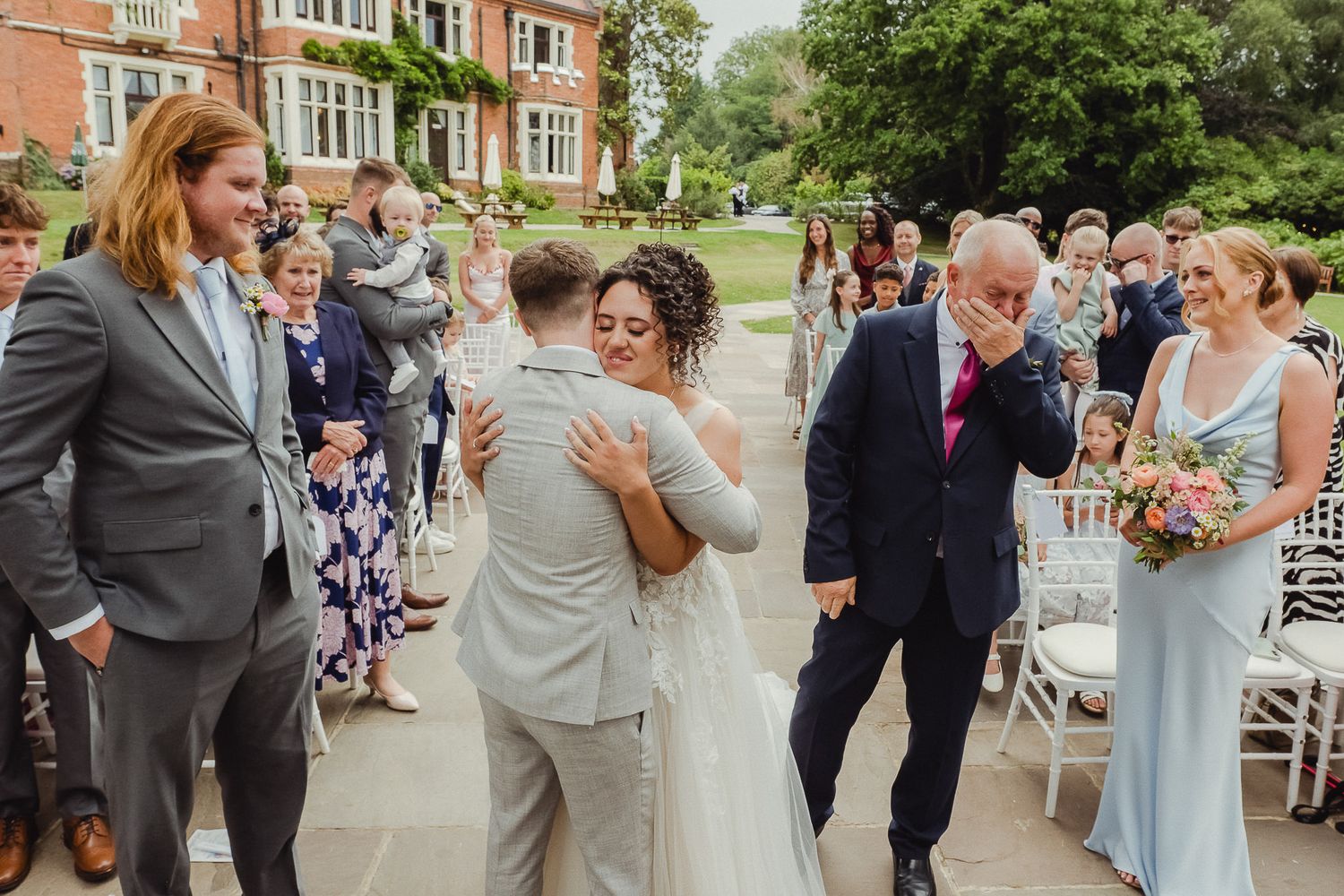 Wedding guests gather and socialize on a paved walkway during an outdoor reception celebration.