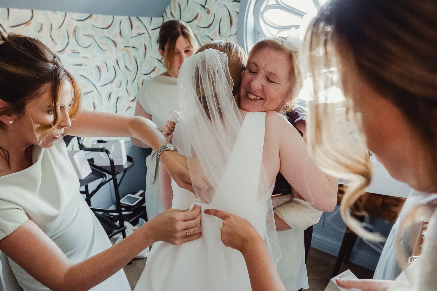 Candid moments of celebration and embraces during wedding preparation indoors.