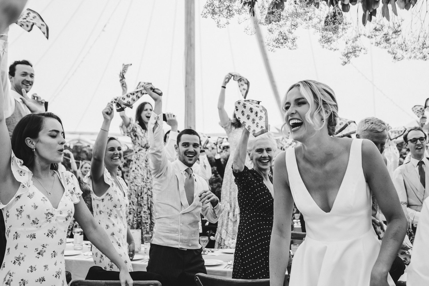 Wedding celebration with guests dancing and cheering under outdoor tent.