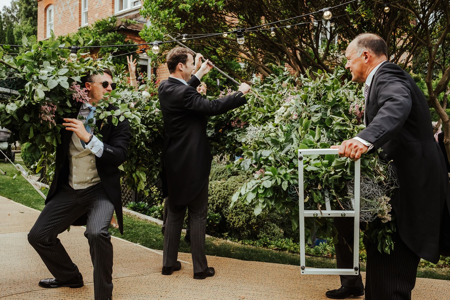 Outdoor wedding reception with guests mingling among garden landscaping and trees.