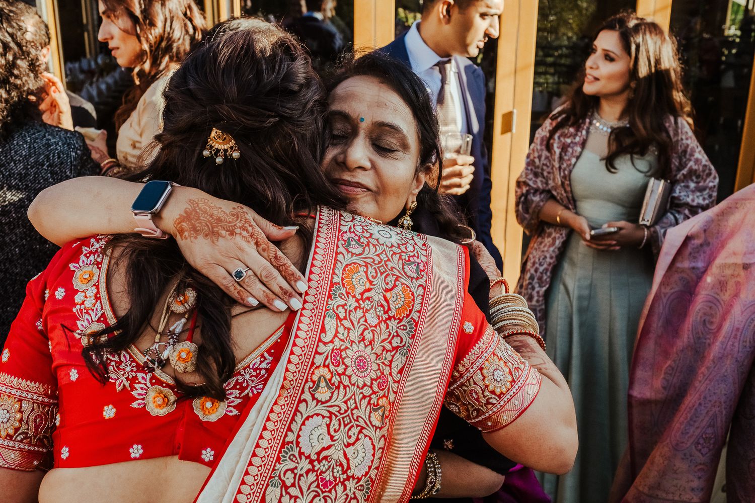 Emotional embrace between guests wearing traditional Indian sarees at an outdoor wedding celebration.