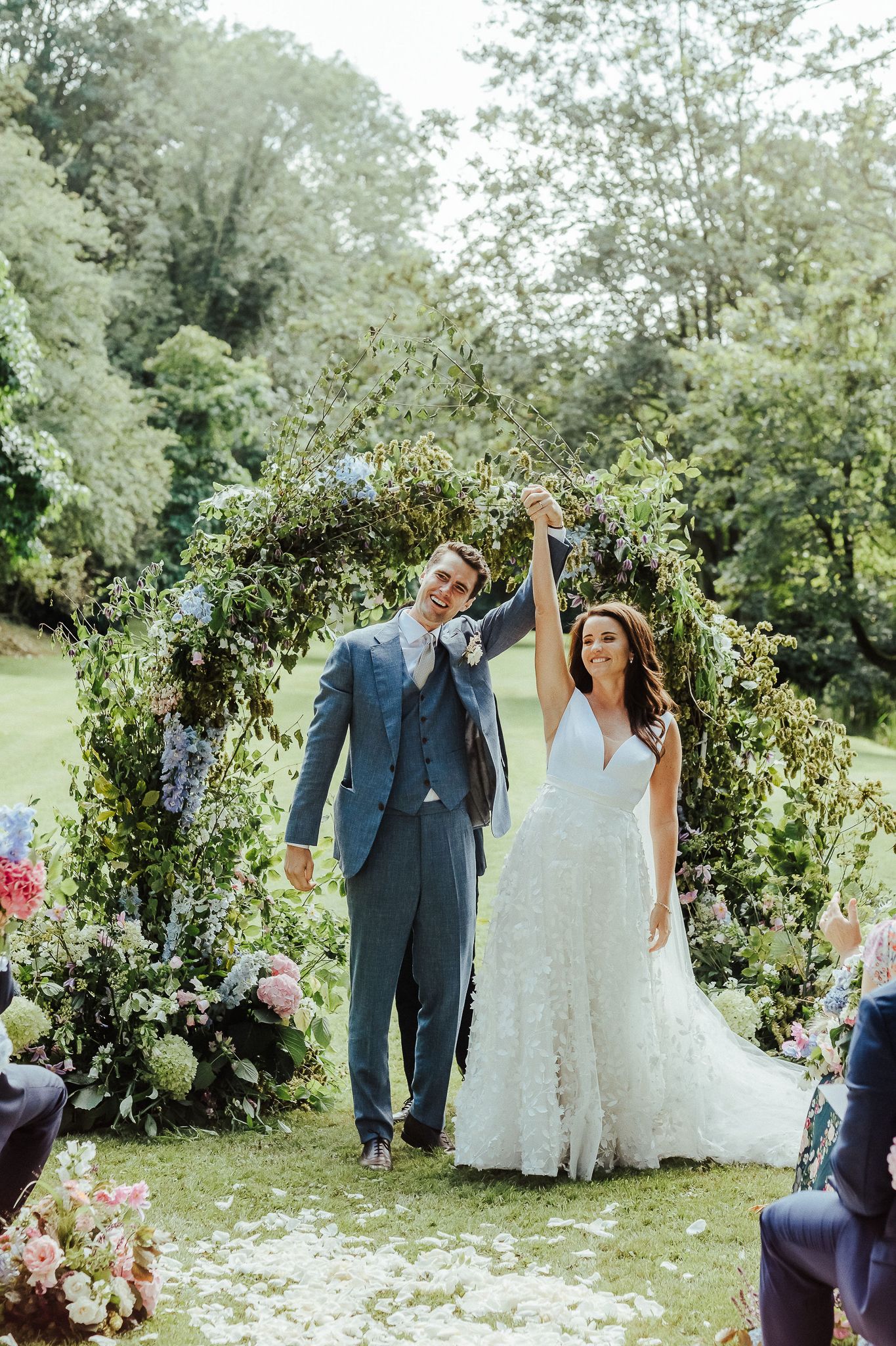 Happy couple celebrates under floral arch after outdoor garden wedding ceremony.