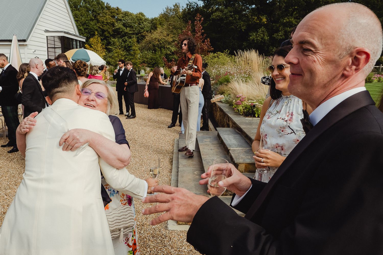 A group of wedding guests raise champagne glasses in celebration outdoors at a rustic venue.