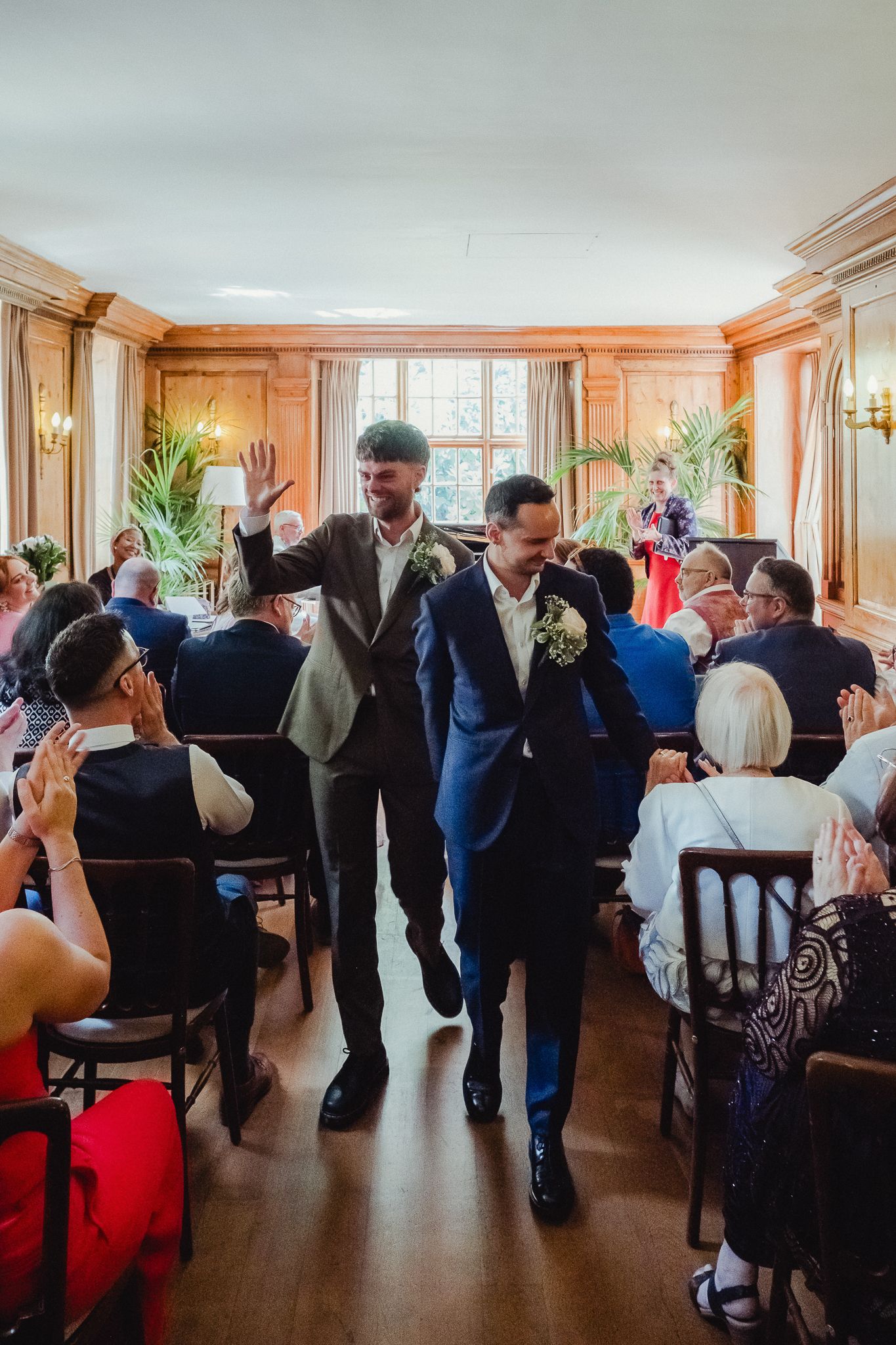 People dancing and socializing at an elegant indoor venue with wooden paneling and large windows.
