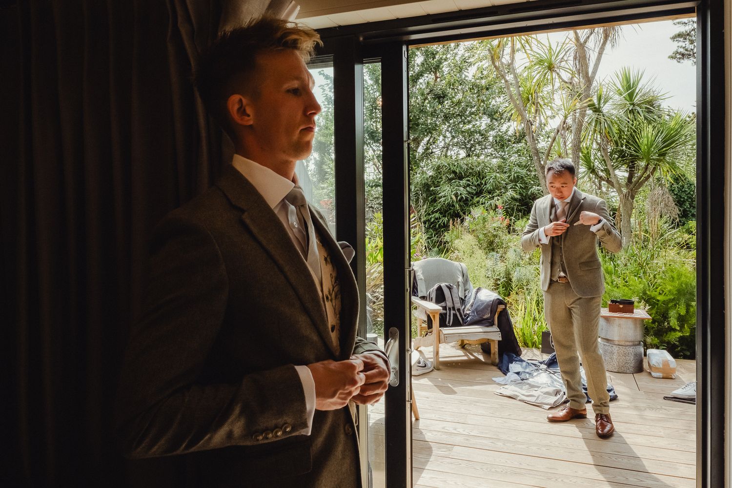Elegant wedding couple shares their first dance in a sunlit venue with large windows and tropical plants.