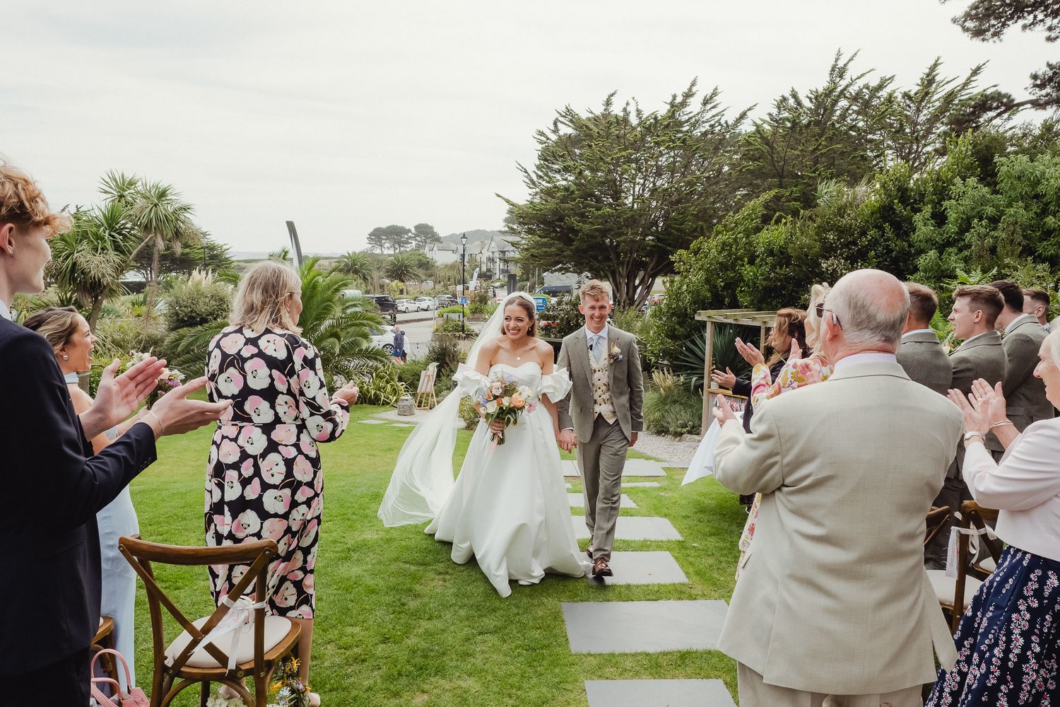 A joyful outdoor wedding ceremony on a grassy lawn with guests watching the couple walk down the stone path.