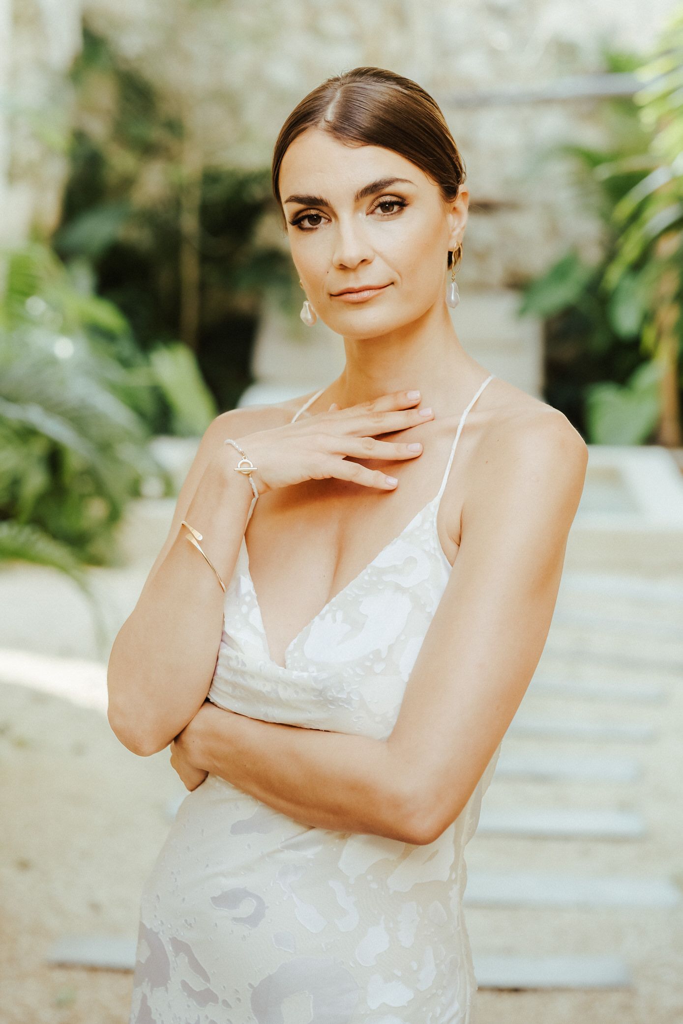 Woman in white lace dress poses elegantly in garden setting with soft natural lighting.