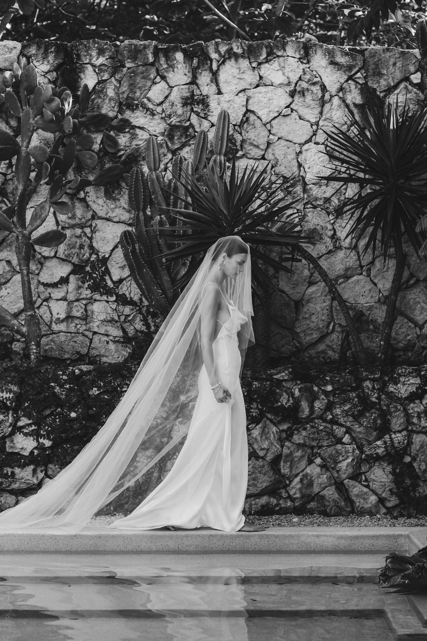 A sequence of black and white photos showing a bride in a flowing wedding gown and veil against a stone wall.