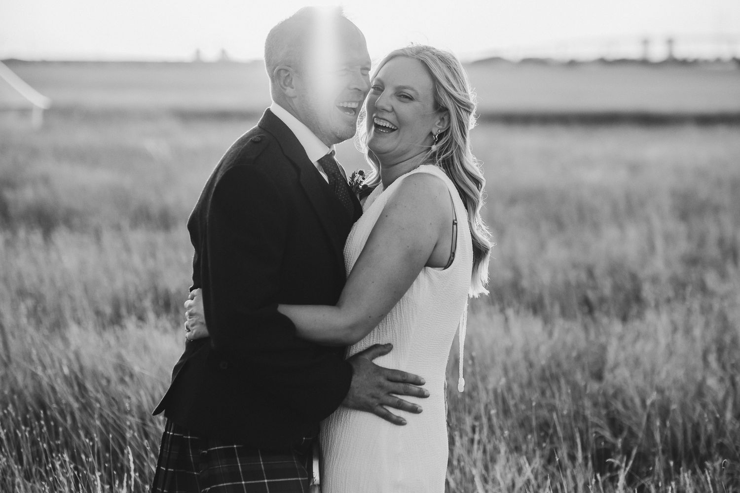 Black and white wedding photos showing romantic moments between a couple in an outdoor field at sunset.