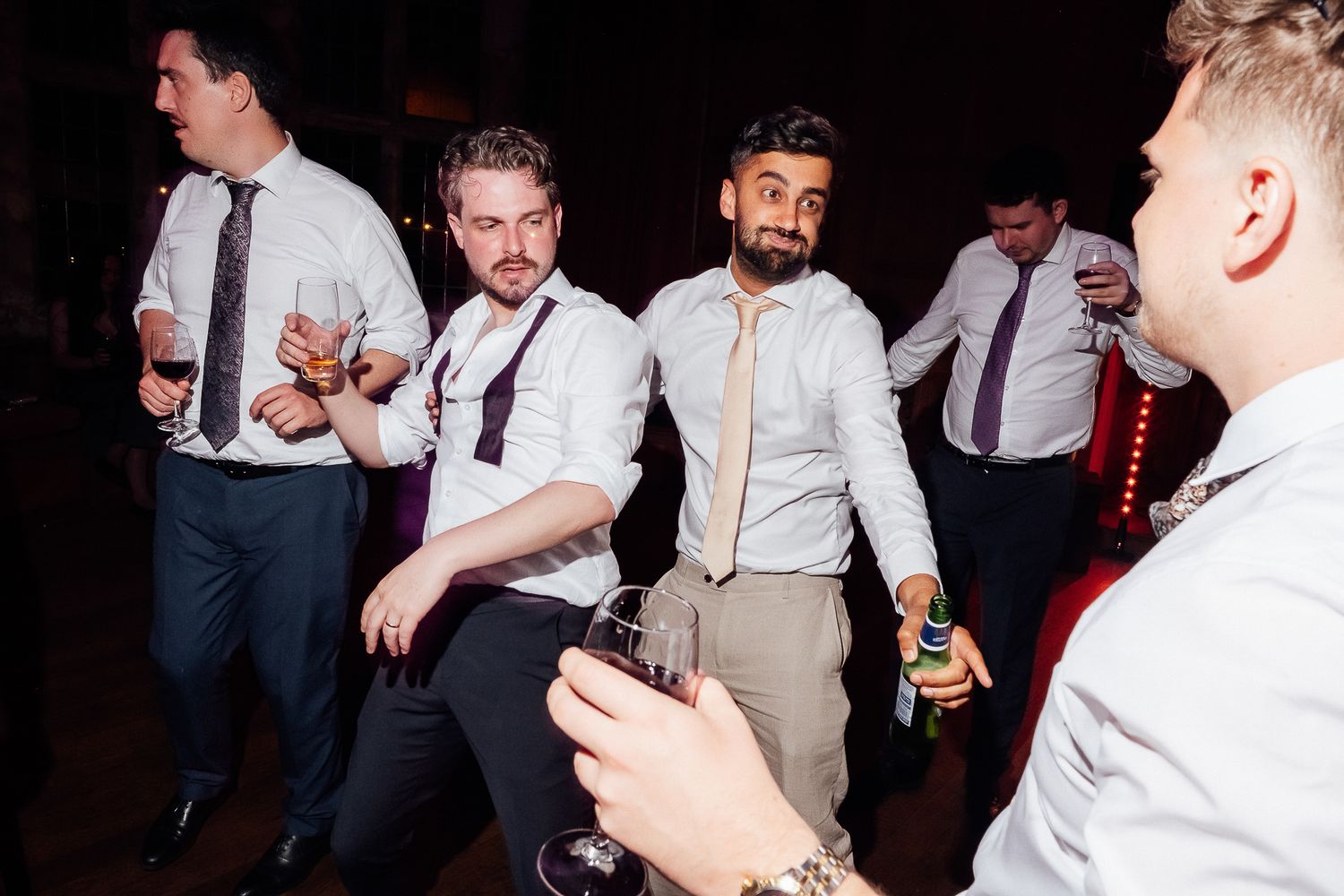 Men in dress shirts and ties dancing and socializing at a formal party or wedding reception.
