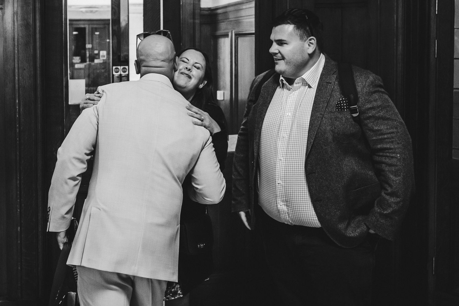 Three people interact near a doorway in a black and white candid photograph.