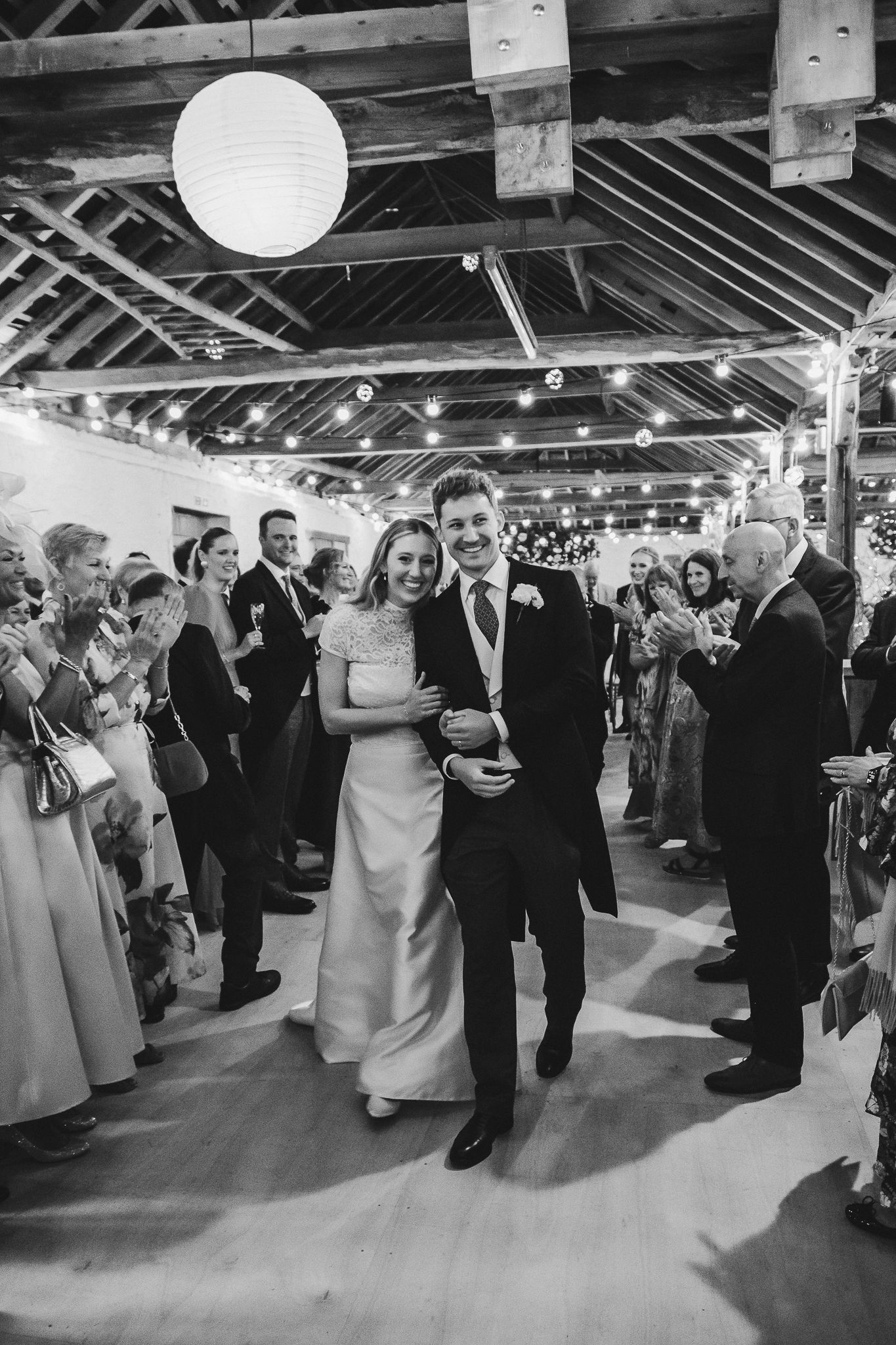 Wedding guests dancing and socializing during a reception under paper lanterns in a rustic venue.