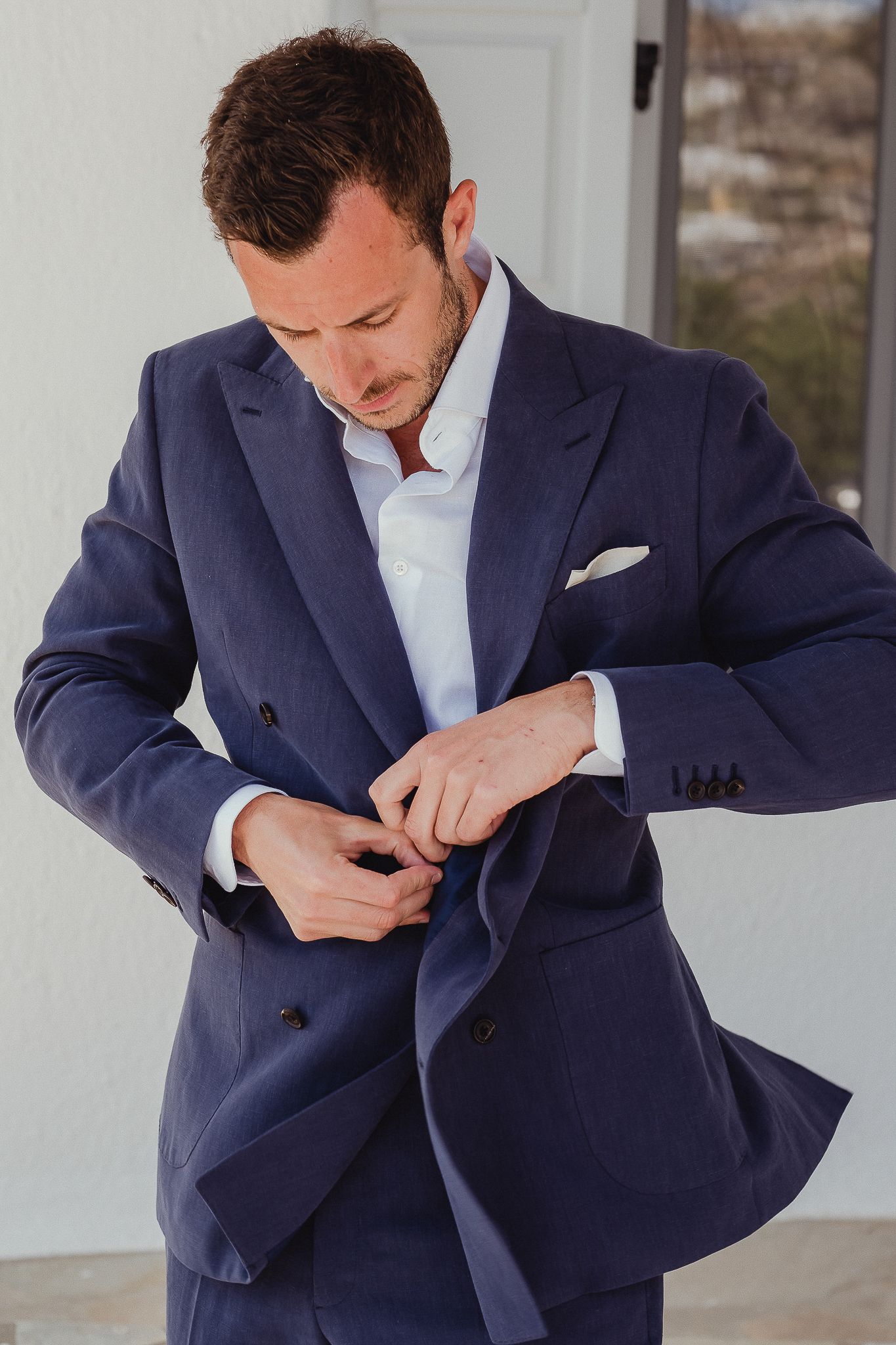 Man wearing navy blue double-breasted suit with light blue dress shirt adjusts his buttons.