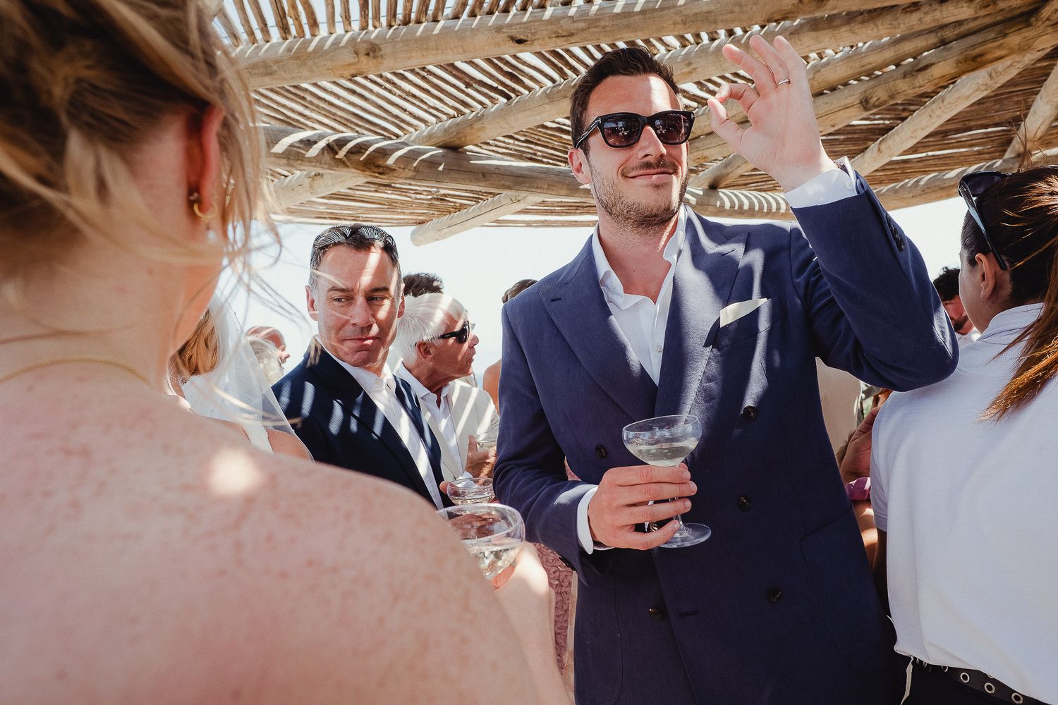 A group of people celebrating and making a toast at an outdoor reception under a timber framed structure.