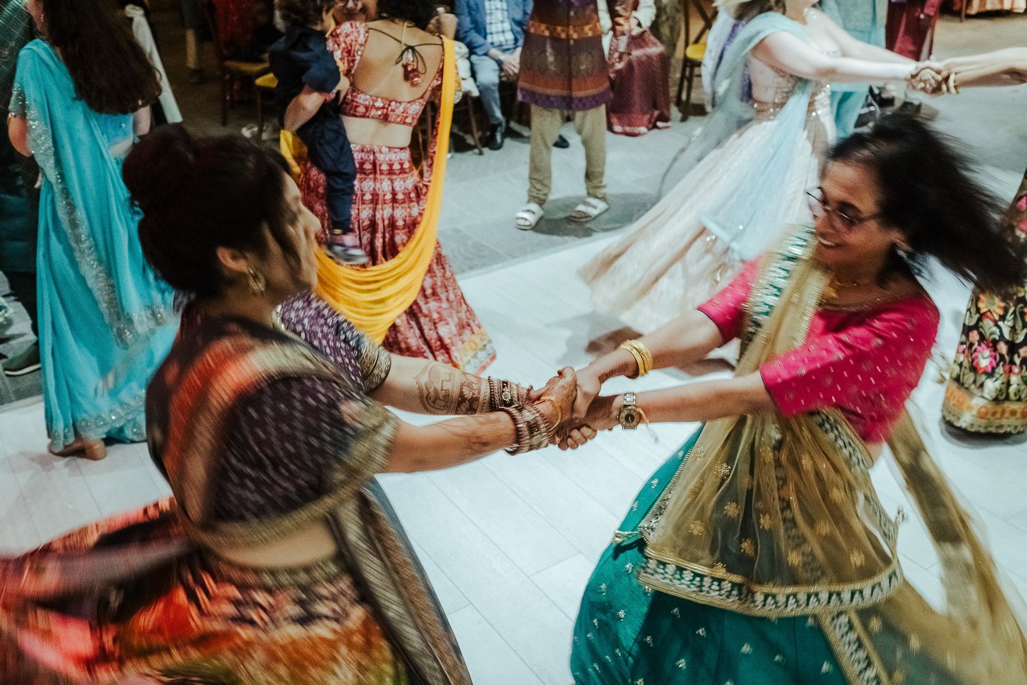 Traditional Indian dancers in colorful saris hold hands in a circle formation.