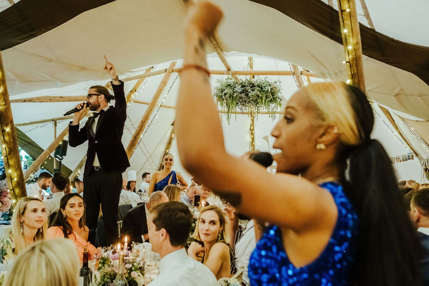 Wedding guests dance joyfully under a white tent during a lively reception celebration.