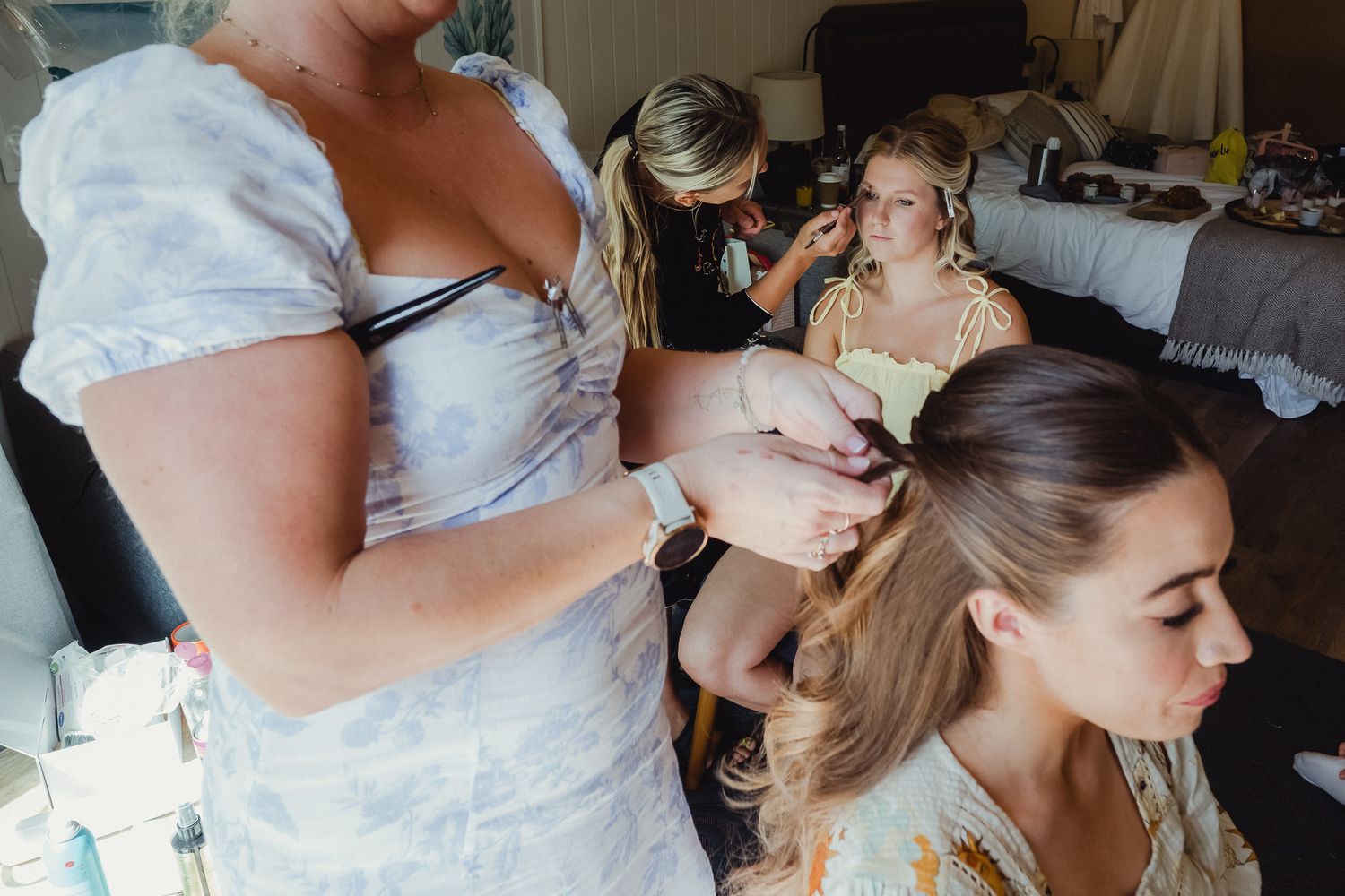 A wedding party getting ready in a bridal suite with stylists working on hair and makeup preparations.