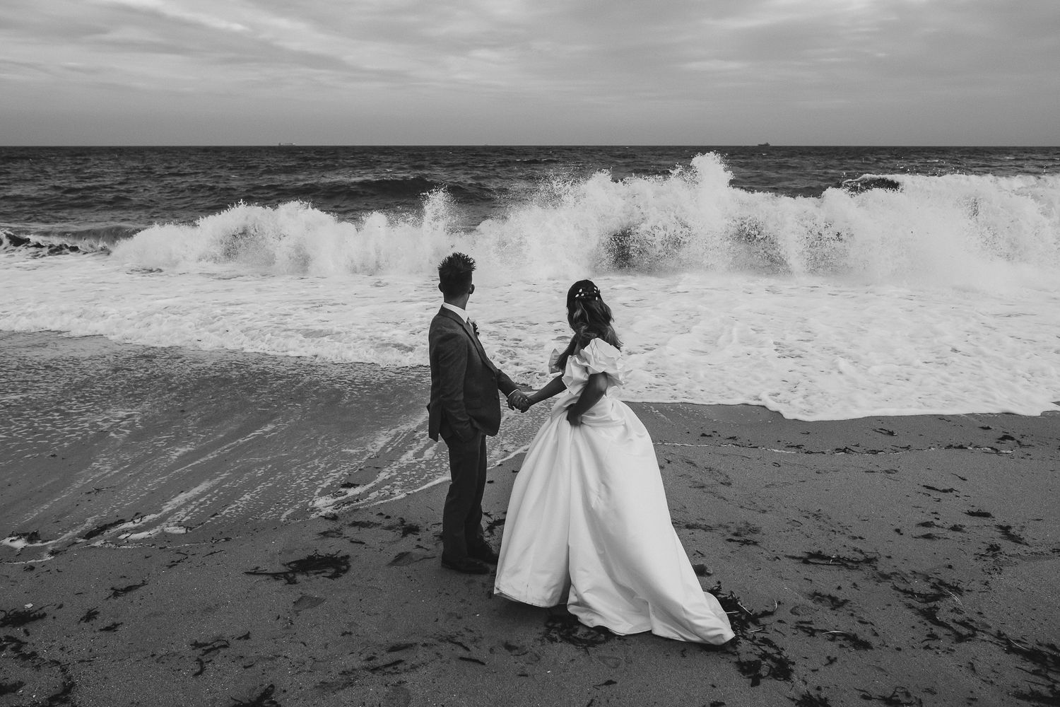 A black and white photo sequence shows a large wave crashing onto a beach where people are standing near the water.