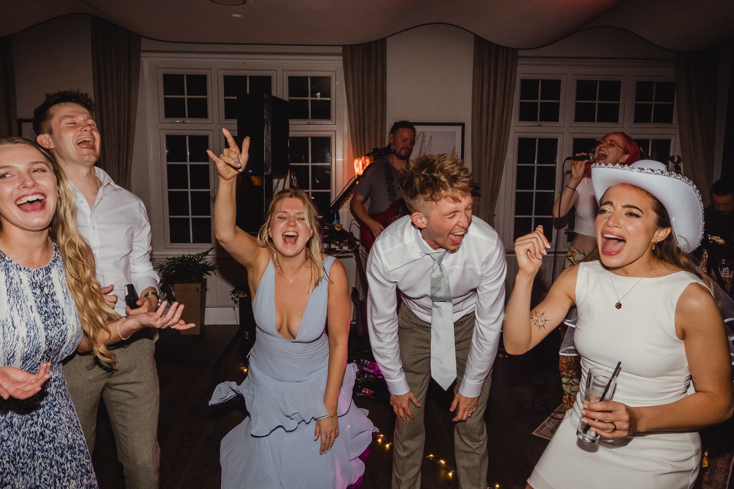 Wedding guests dance and celebrate joyfully on the dance floor at an indoor reception venue.