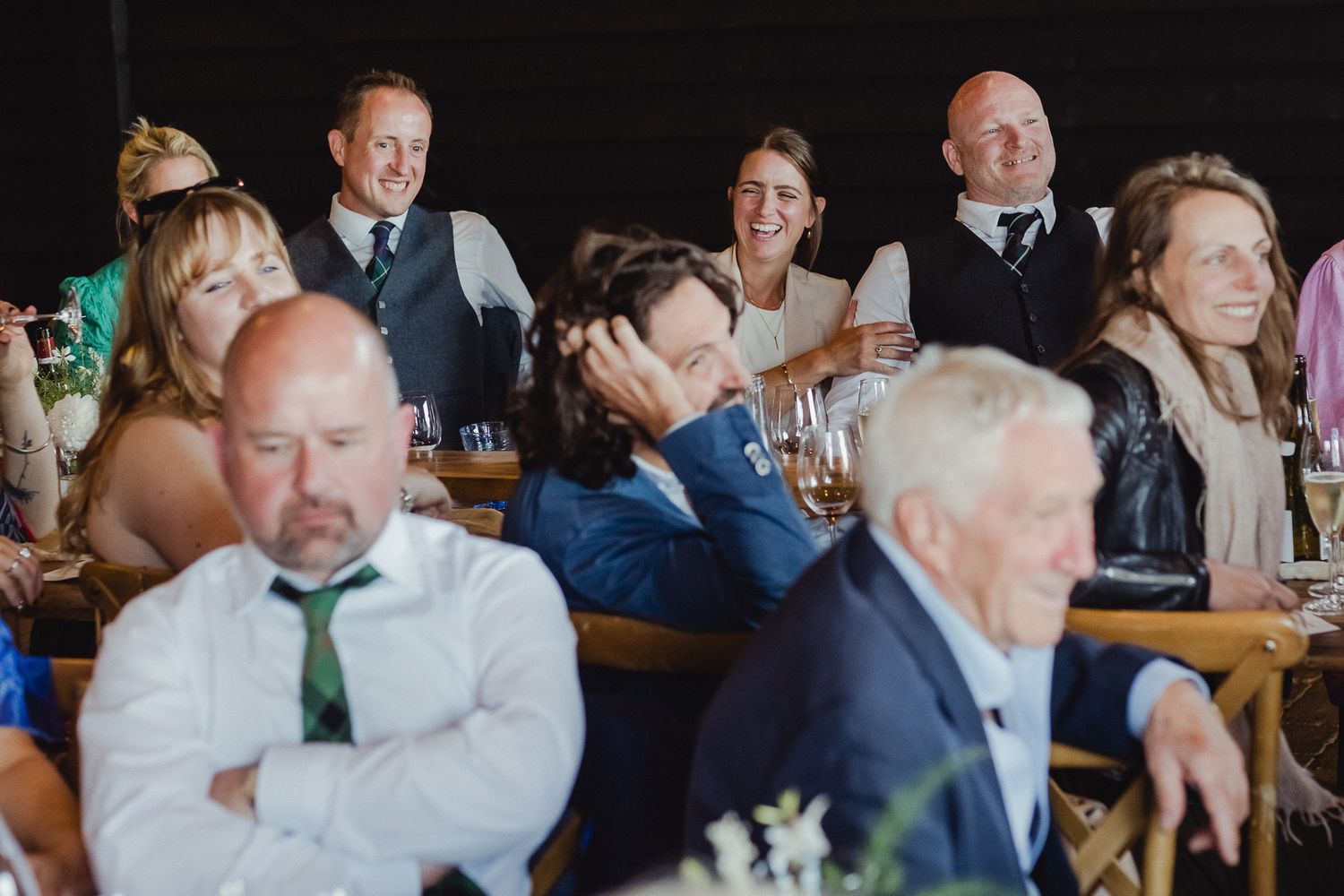 Wedding guests listen attentively during speeches at an indoor reception venue.