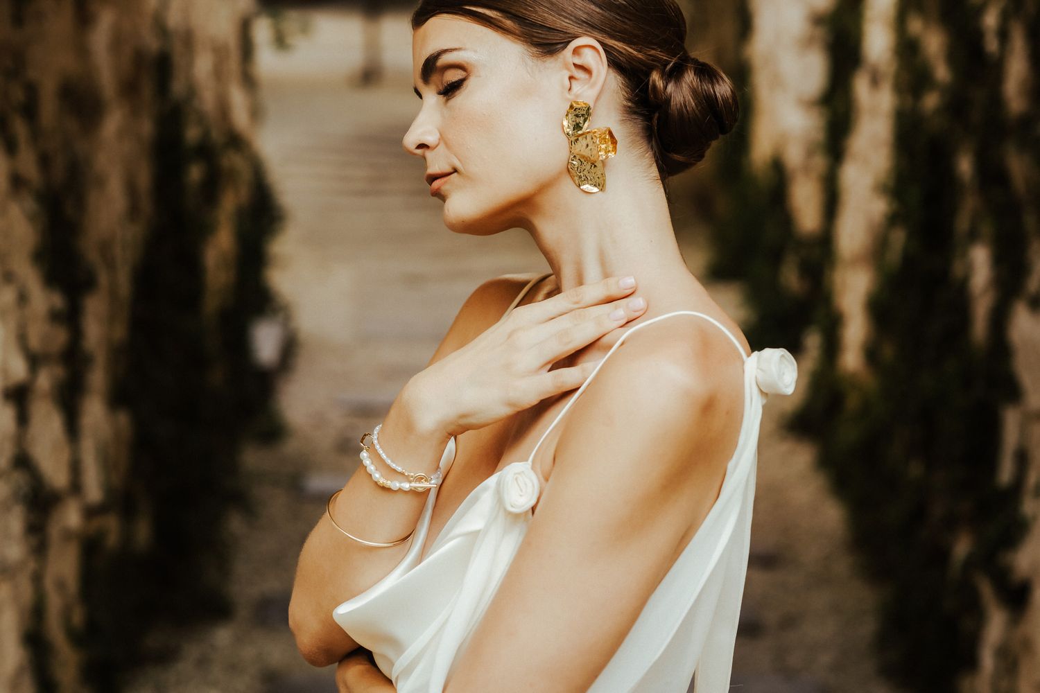 A person in an elegant white dress poses gracefully against a rustic wooden backdrop in natural lighting.