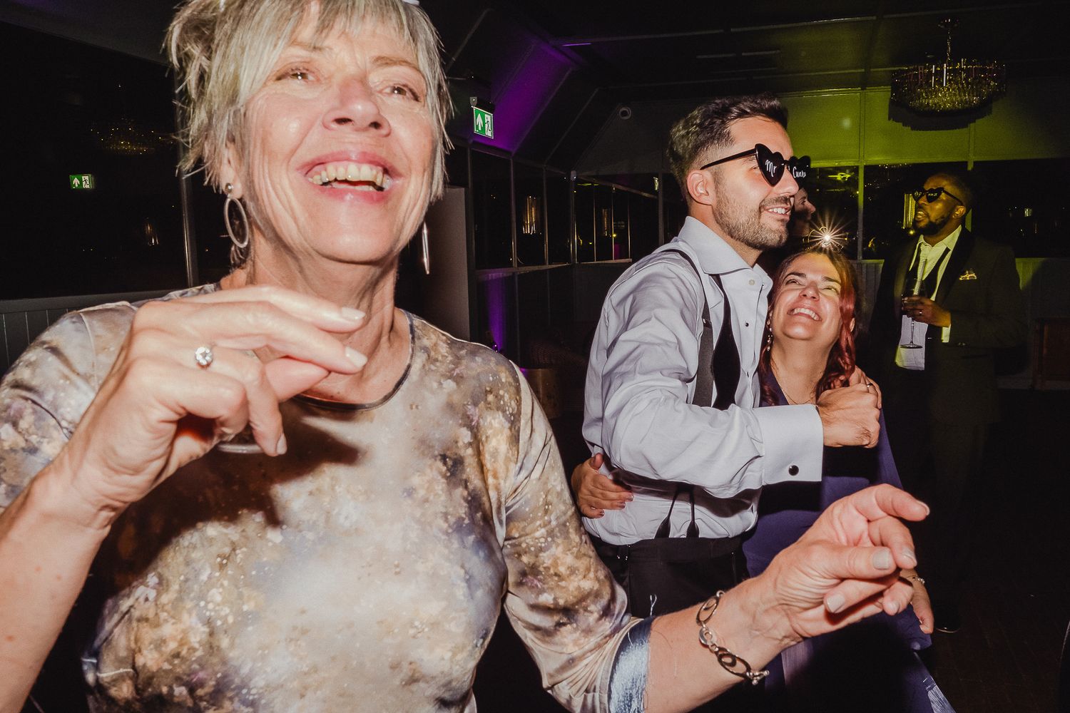 Wedding reception guests dancing and celebrating on a dimly lit dance floor at a party.