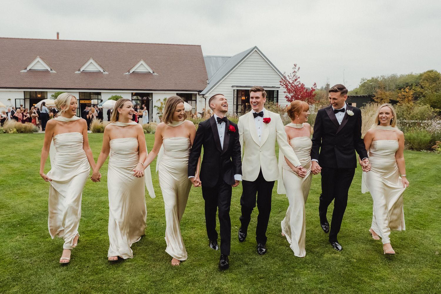 Wedding party members walk together across a grassy lawn in formal attire during an outdoor celebration.