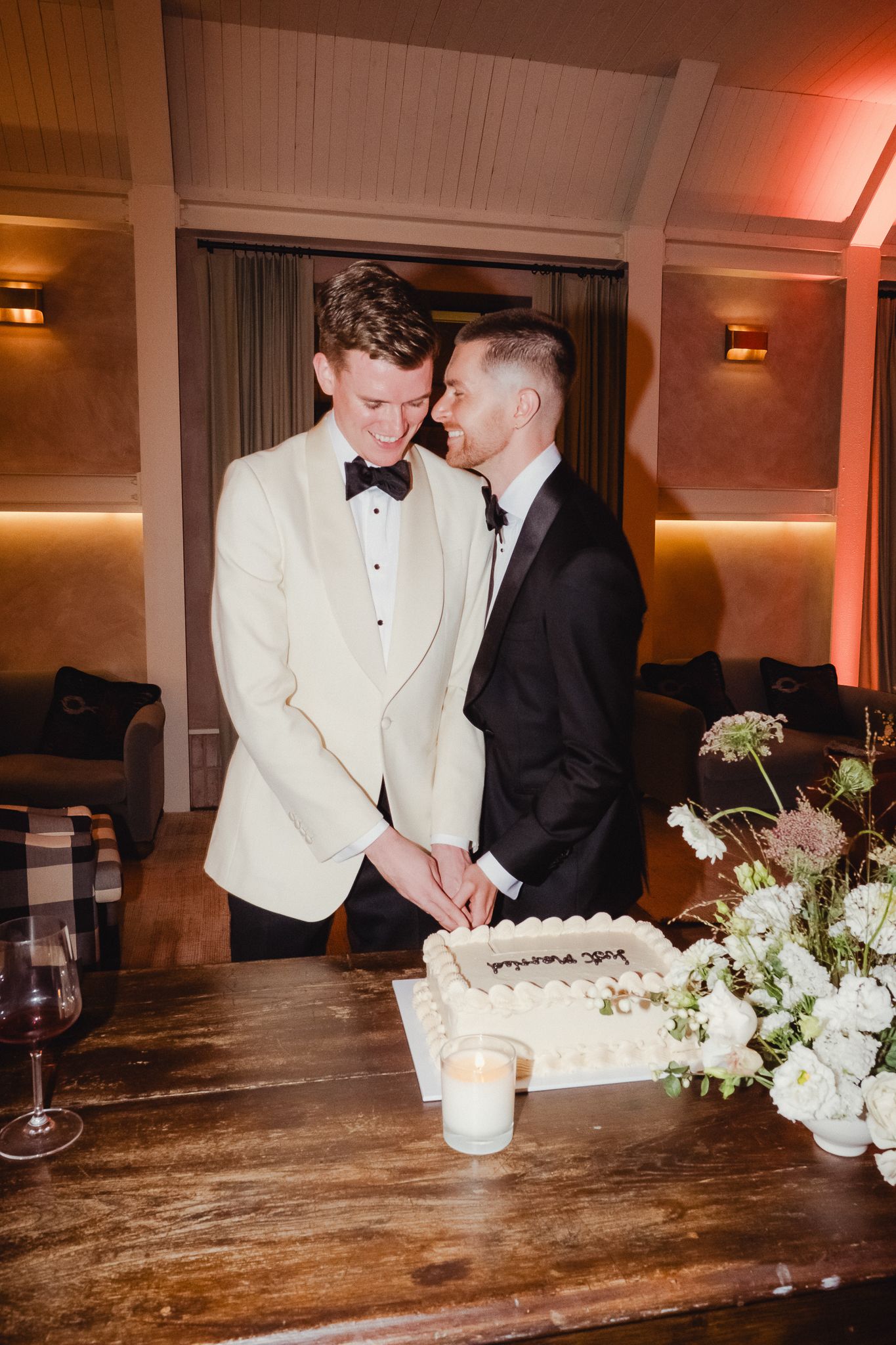 Two people in formal attire share a sweet moment while cutting their wedding cake at an elegantly decorated reception.