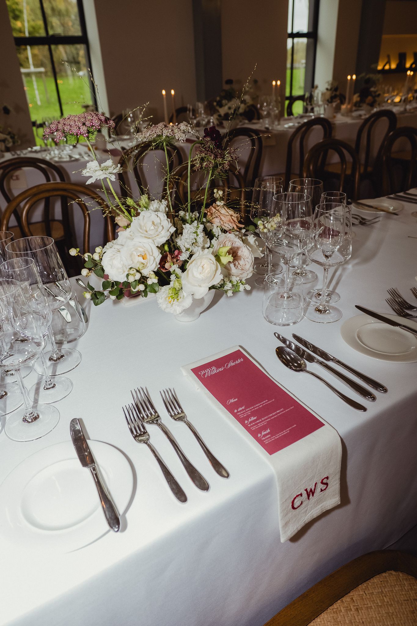 Elegant wedding table setting with white linens, crystal glasses, and pink menu cards decorated with delicate floral arrangements.