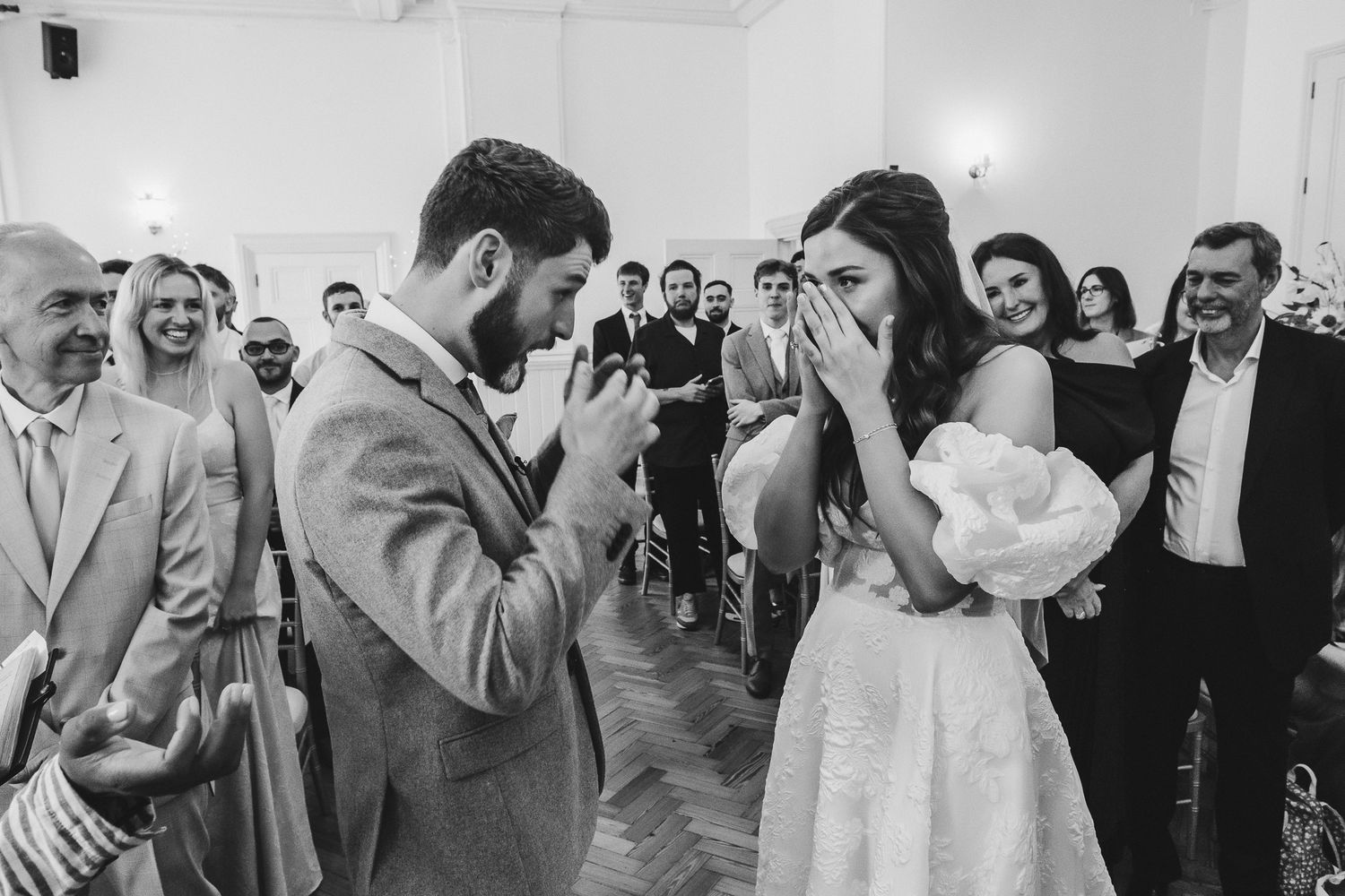 Wedding reception guests form a dancing circle during a lively celebration in a bright white venue.