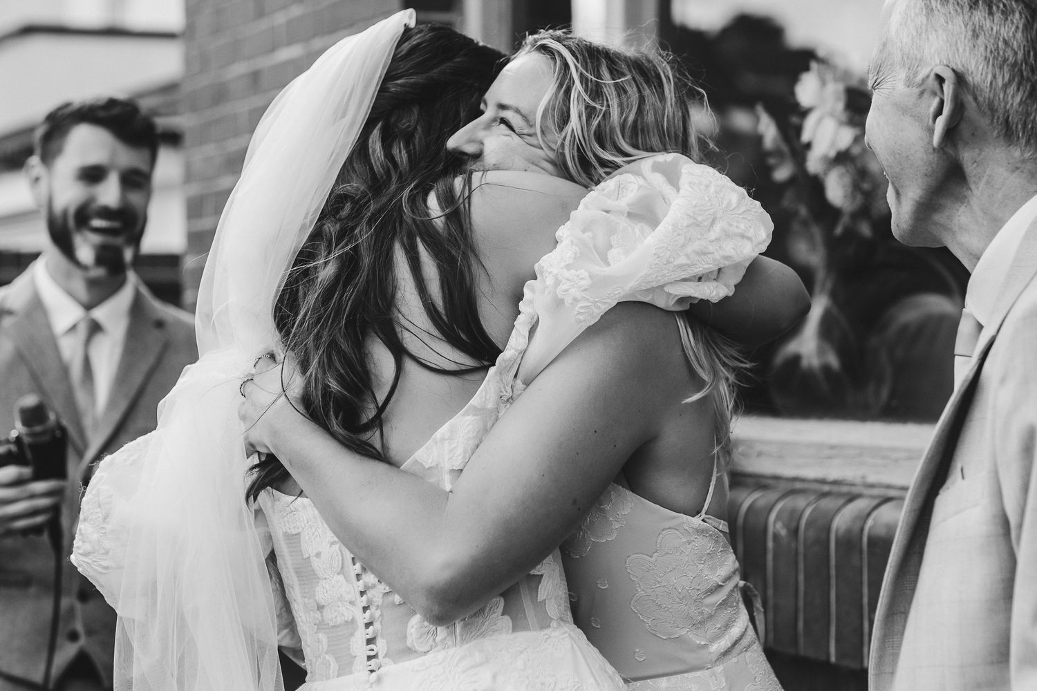 An emotional embrace between two people at a wedding celebration, captured in black and white photography.