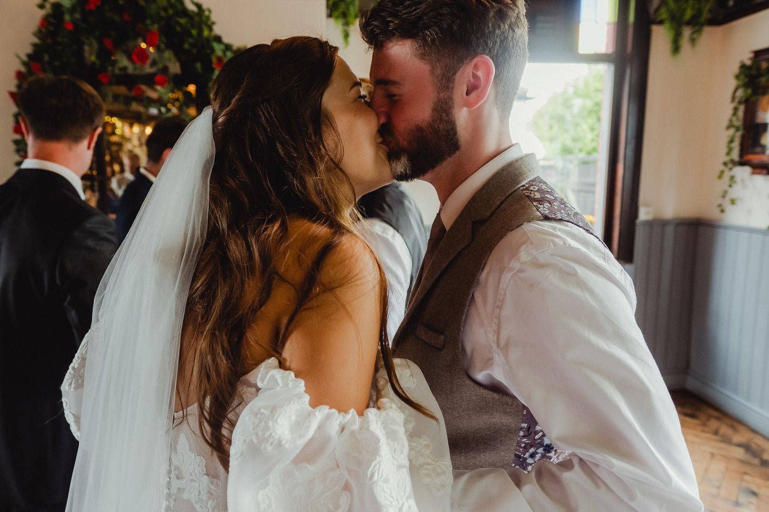 Newlywed couple shares a romantic kiss during their wedding reception while surrounded by holiday decorations.