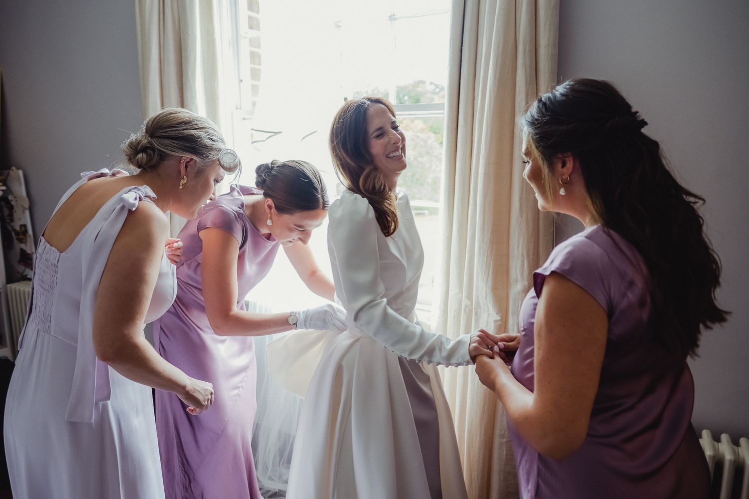 Wedding party members help with final preparations in a sun-lit room before the ceremony.