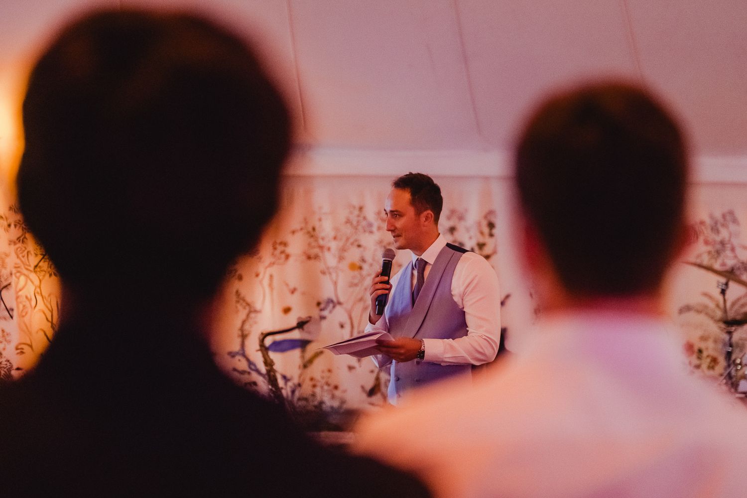 A wedding ceremony in a modern venue with white floral decorations and soft pink lighting.