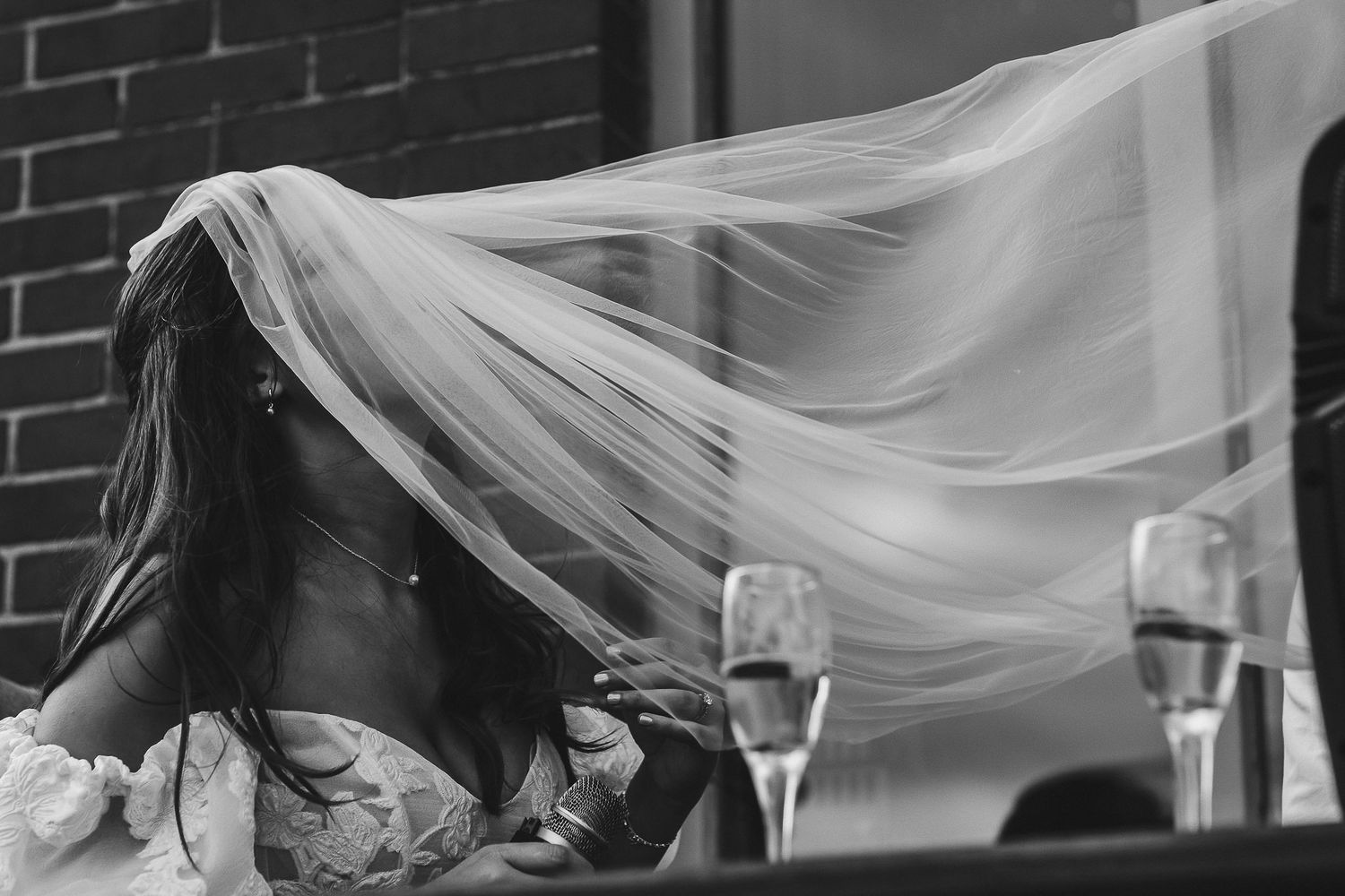 A flowing white wedding veil billows in the breeze next to two champagne glasses on a table.