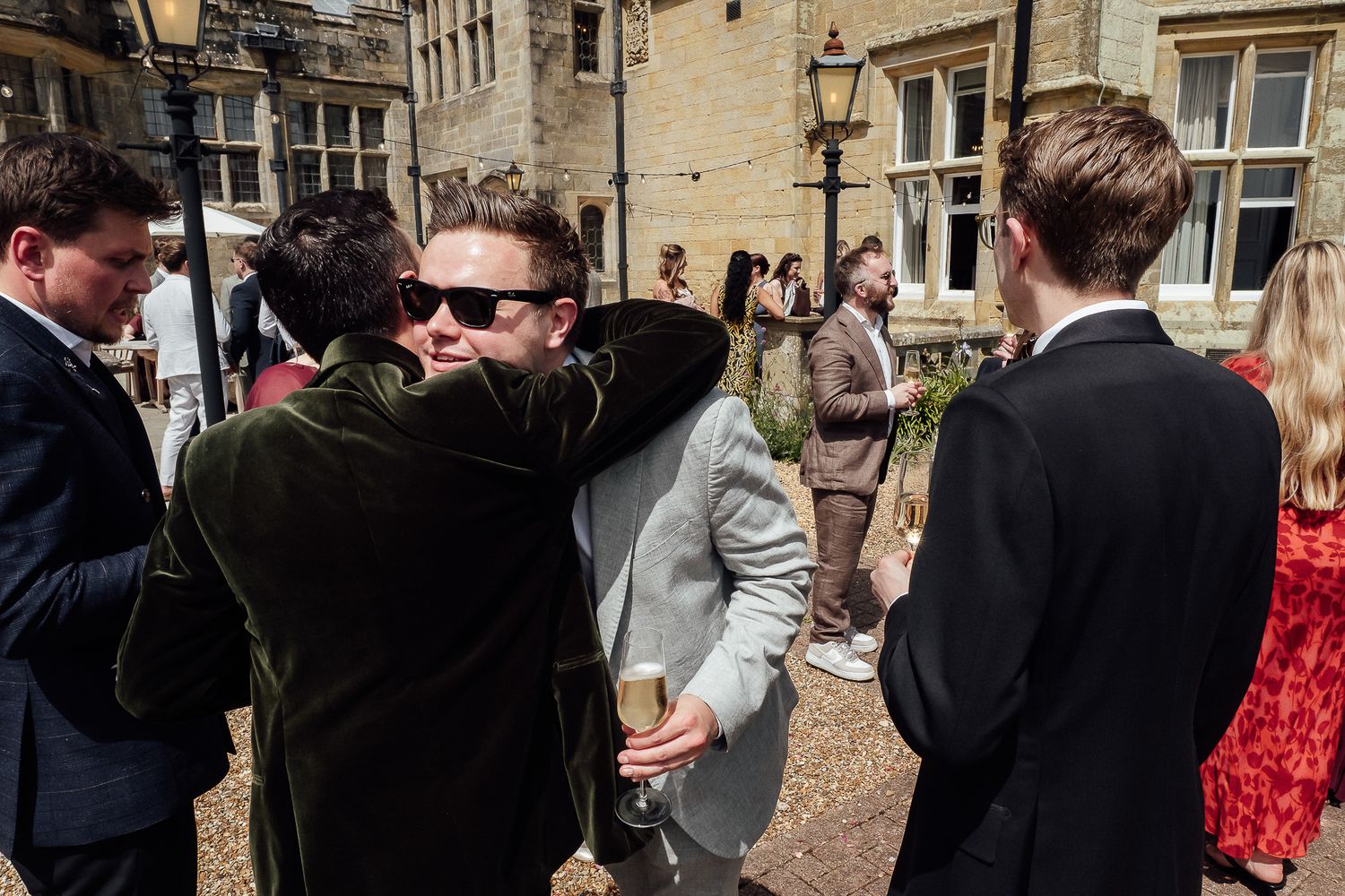 Guests socializing outdoors at a formal event near a historic stone building on a sunny day.