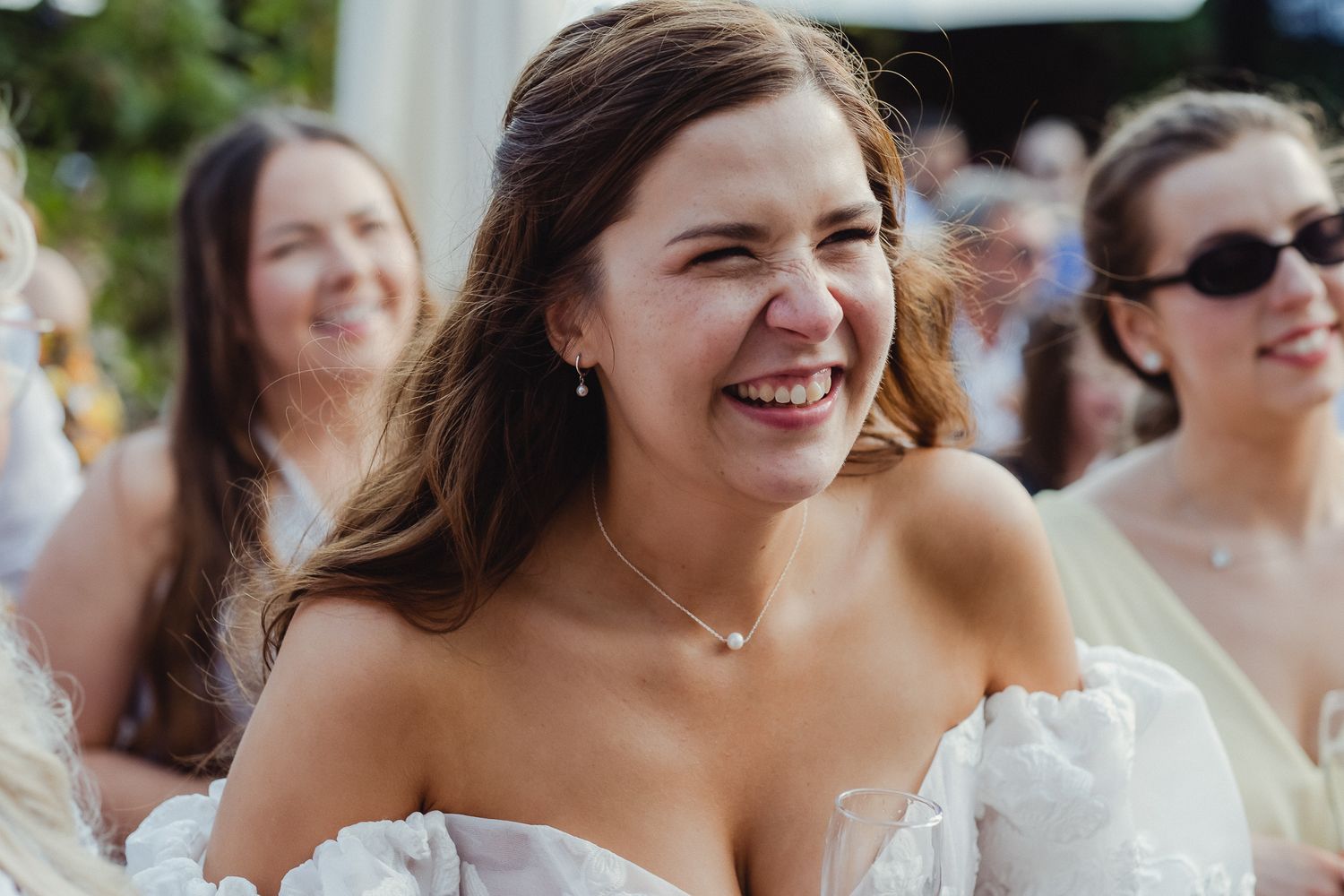 A group of wedding guests share joyful laughter during an outdoor celebration.